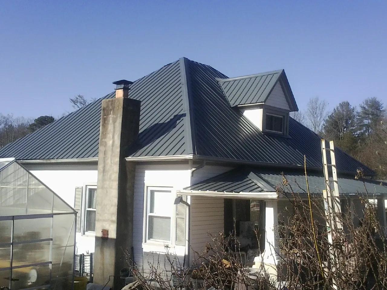 Dark blue standing seam metal roof on a white farmhouse with dormer — Slate & Tile Roof Repair by Roofing Brothers in Coloma