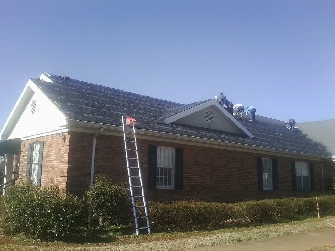Crew tearing shingles off a brick ranch roof with a ladder set — Emergency Roof Repair work by our crew in Coloma