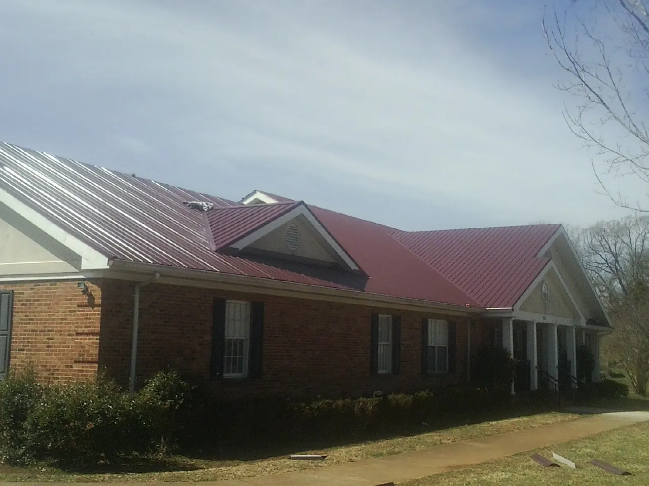 Red metal roof with gabled entries on a long brick building, from a Hail Damage Roof Repair job in Coloma