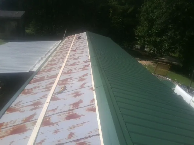 Old rusted panels beside newly installed green metal roofing — Wind Damage Roof Repair by Roofing Brothers in Coloma