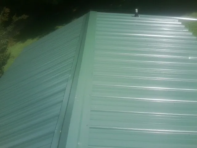 New green metal panels meeting at the ridge of a roof — Flat Roof Repair work by our crew in Coloma