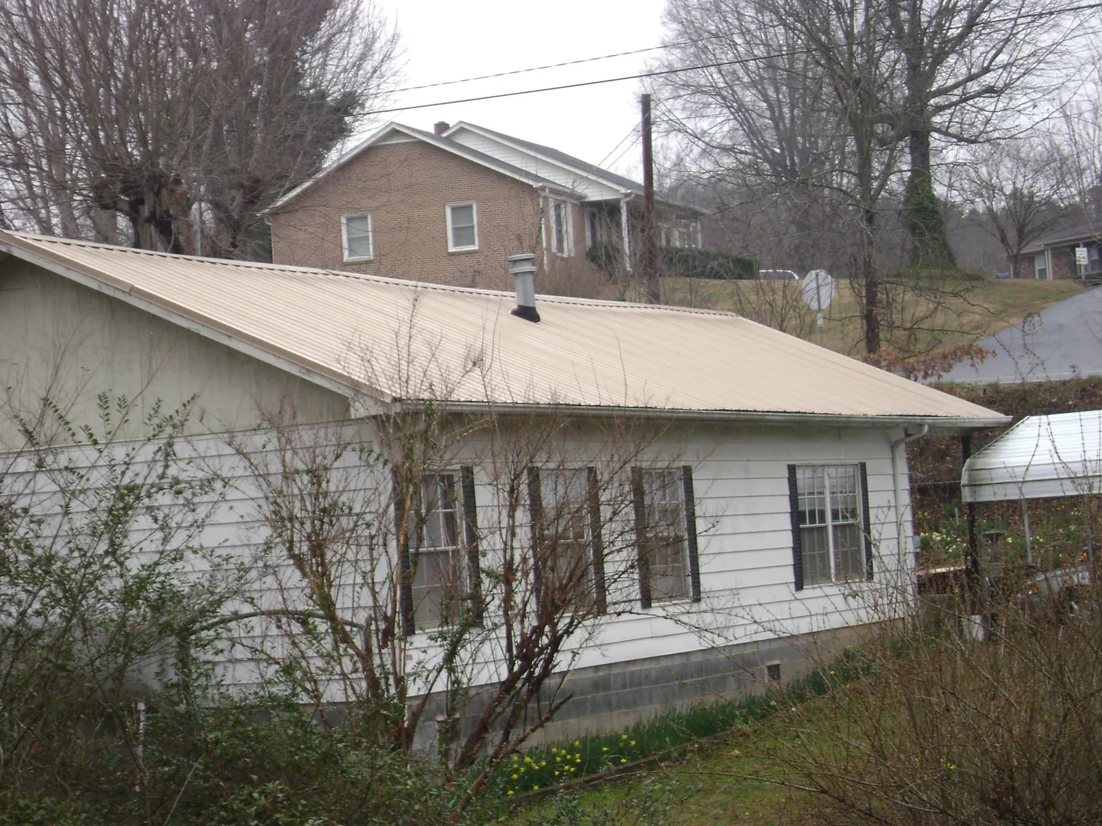 Tan metal roof on a white sided house set into a hillside — Commercial Roofing by Roofing Brothers in Coloma